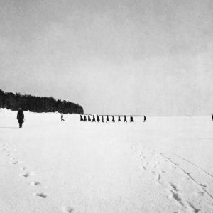 Svartvitt foto från 1921. Svarta skepnader på havsisen nära stranden. De första flyktingarna kommer.