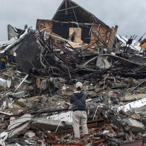 En man står med armarna i kors och tittar på ett hus som rasat ihop i Mamuju, Indonesien.