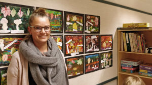 Filippa Belfrage. Filippa Belfrage står framför en anslagstavla med kollage som förskolebarn har gjort.