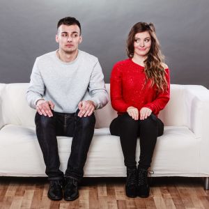 Ung man och kvinna sitter i en soffa och sneglar på varandra
