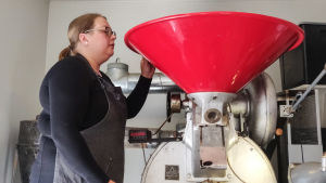 De råa bönorna åker ner i tratten. Mellan 20 och 22 kilo bönor rostas på en gång. En kvinna tittar ner i en stor röd tratt ovanpå en kafferost.