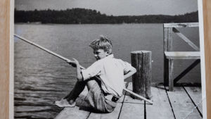 Caj som liten pojke. Svartvitt foto av Caj Bremer som barn som sitter och metar på en brygga.