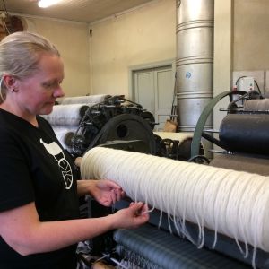 Den andra kardningsmaskinen formar ullen till rullar. Kvinna vid kardningsmaskin