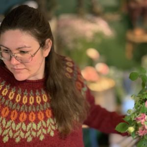 En kvinna med stickad tröja står med en blombukett i handen