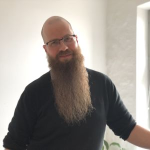 Porträtt av en man med långt skägg och mörk tröja. 