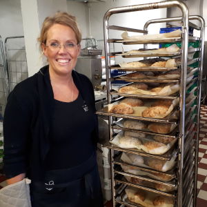 Brödet bakas på surdeg. Malin Furu har precis lyft dagens glutenfria bröd ur ugnen. Kvinna bredvid en ställning med nybakade bröd.