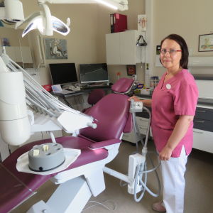 En kvinna, tandläkare, i rosa arbetsrock och vita byxor står vid en rosa tandläkarstol.