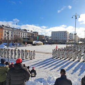 Solen lyser över tiotals beväringar som deltar i försvarsmaktens paradmönstring på Vasa torg. I förgrunden publik som samlats. 