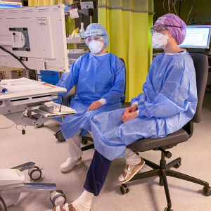 Två sjukskötare i blå skyddsförklädena betraktar monitorer på intensivvårdsavdelningen.