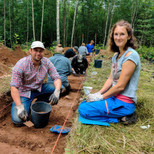 En man och en kvinna sitter vid ett sanddike vid en arkeologisk utgrävning.