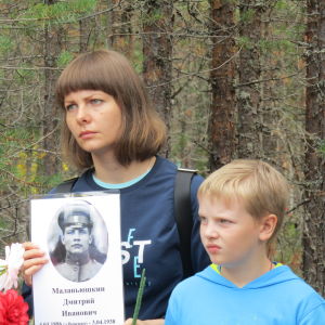 En kvinna och en pojke håller upp en bild på en soldat.