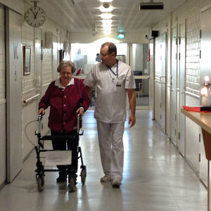 Närvårdare Karl-Erik Dahlin går genom korridoren med Doris som går med rullator.