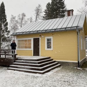 Man står på trappan till litet hus i snöstorm.