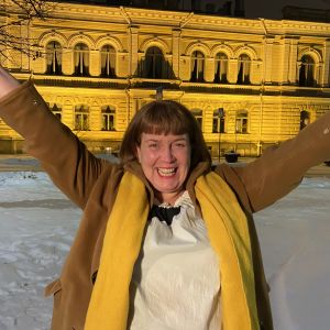 En glad kvinna sträcker upp händerna i en segergest. Bakom henne syns Borgå stadshus.