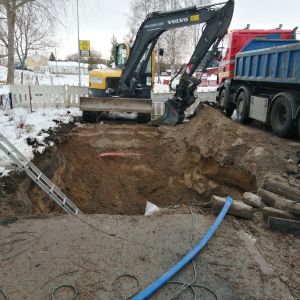 En stor och djup grop mitt i en väg i centrum av Ingå. Vattenledning som gått sönder. Grävmaskin och lastbil på plats. En lekpark till vänster om vägen.
