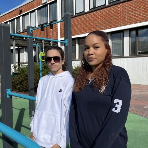 En pojke och en flicka står framför en klätterställning, i bakgrunden en skolbyggnad i tegel.