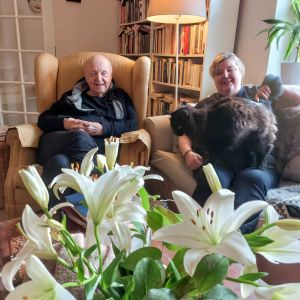 Katten Felix i Carina Nynäs famn. Hon sitter i soffan och bredvid henne i en länstol sitter hennes man Lars Bergquist.