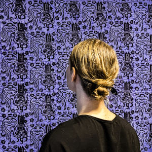 En kvinna står framför ett blått tyg med ansiktet frånvänt.
