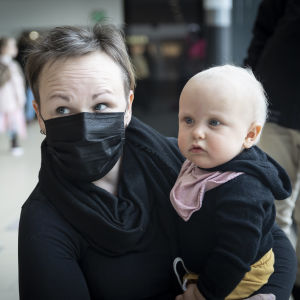 Tiina Ranta-Panula funderar en hel del på hur Kerttu påverkas av att hennes sociala kontakter begränsats så mycket. Tiina Ranta-Panula iklädd munskydd håller dottern Kerttu i famnen.