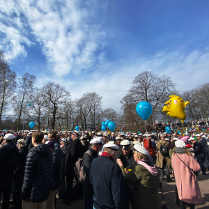 Folkmassa med många studentmössor i Kajsaniemiparken, med en Pikachu-ballong och blå himmel.
