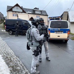 Kolme mellakkavarusteisiin pukeutunutta poliisia seisoo kadulla.