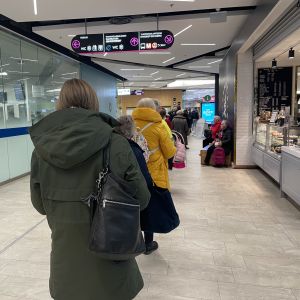 En lång rad människor står i kö i en gång i ett köpcentrum.