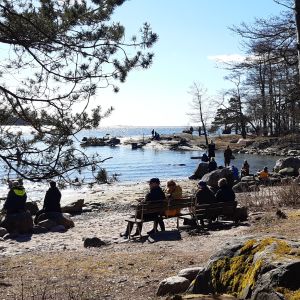 Den långa kustremsan lockar storstadsbor som gärna sitter en stund i solen. I söndags 5 april såg det ut så här. Många människor på sandstranden på Drumsö varav en del sitter på parkbänkar