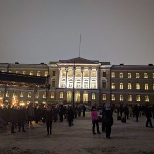Helsingin yliopiston päärakennus iltahämärissä, etualalla suuri yleisöjoukko.