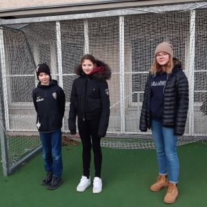 Bastian Lindberg, Sandra Maurizi och Emmi Lumio funderar om kallt väder och att vi vänjer oss vid att sitta stilla kan vara orsaker till varför vi rör på oss mindre. En pojke och två flickor står framför ett fotbollsmål på Åshöjdens skolgård och tittar in i kameran.