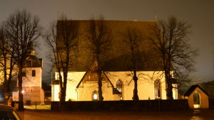 Det är bara ett stenkast från Biskopsgården till Borgå domkyrka. Borgå domkyrka upplyst av lampor i mörkret. Det är en stor vit stenbyggnad med mörkt spåntak.