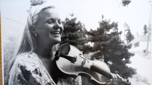 Raakel Lignell övade violin 8-10 timmar per dag. Svartvitt foto av Raakel som leende håller i fiolen.