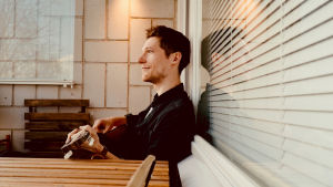 Månskensbonden aka Markus Bergfors med gitarren i famnen på sin balkong. Musikern Månskensbonden sitter på sin balkong med gitarr i famnen.