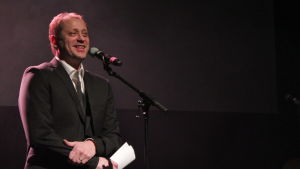 Lars Backlund, Cecilias far, överraskar med humor. En man som står på en scen iklädd kostym.