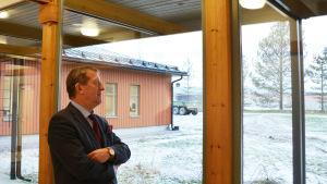 Gången mellan den nya och den gamla delen av kontorshuset har en vägg nästan helt gjord av glas. Bakom vd Patrik Wackström synns den delen av huset där han själv har sitt kontor. Bakgården ska ännu få buskar och andra växter. Medelålders man i kostym står med armarna i kors och tittar ut genom ett stort fönster. Bakom honom synns genom fönstret en tom gårdsplan och en del av det röda huset.