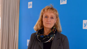 Marianne Pekola-Sjöblom, Kommunförbundet. Marianne Pekola-Sjöblom står framför en blåvägg med Yle-logon.