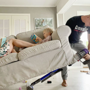 Carro ligger i soffan med sin dotter som läser bok. Carros man lyfter soffan så halva är i luften medan han dammsuger under soffan.