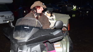 Martina Bergström får en våt morgonpuss av sin hund. Tillsammans åker de sedan fyrhjuling för att samla ihop får till fredagens första starter. En kvinna i hatt och en hund på en fyrhjuling. Det är mörkt som på natten ute.