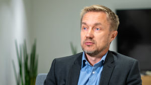 Hoas fastighetsdirektör Kim Lindholm påpekar att studentbostäder slits extra mycket eftersom så många studerande flyttar in och ut varje år. Direktör iklädd kavaj och kragskjorta sitter i ett mötesrum och blir intervjuad.