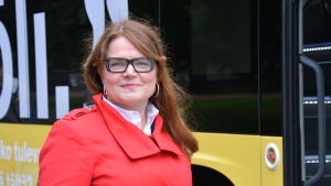 Sirpa Korte vid Fölis dubbeldäckare. Kollektivtrafikchef Sirpa Korte står i röd jacka framför den gula Fölibussen.
