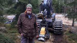 Den milda vintern inverkar på hela samhällets ekonomi. En man står i en skog framför en skogsmaskin.