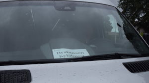 Raseborgs byabuss ser ut som vilken minibuss som helst förutom den här lappen i framrutan. En silverfärgad minibuss med en lapp i framrutan där det står "Byabussen-Kyläbussi".