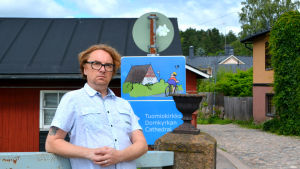 Pertti Jarla vid en av sina skyltar i Borgå. Man står bredvid trafikskylt med bild på cyklist.