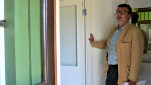Rektor Henrik Grönroos vid den renoverade internatbyggnaden. Man i skjorta oc kavaj står i dörröppningen till en grön träbyggnad.