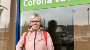 Tryggt och välorganiserat, tyckte Tove Fagerholm om vaccinationsstället i Kyrkslätts centrum. Tove Fagerholm i rosa kappa framför glasdörr.