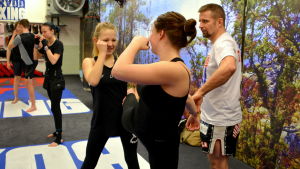 Tränare Mika Pietilä demonstrerar hur flickorna ska öva. Två kvinnor tränar thaiboxning inne i en träningslokal.