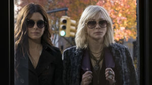 Debbie (Sandra Bullock) och Lou (Cate Blanchett) är coola skurkar med en genialisk plan. Debbie (Sandra Bullock) och Lou (Cate Blachett) står vid ett fönster och tittar in.