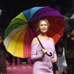 En kvinna i en ljuslila klänning håller i ett paraply i många färger.