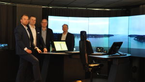 Anton Westerlund, chef för Kongsbergs enhet i Åbo, Markus Laurinen, programchef, Olli Rantanen, vd, Oskar Levander, ansvarig för koncept och innovation. Simulatorn föreställer ett kontrollbord för fjärrstyrning från land. Fyra herrar står kring bordet vid Kongsbergs fartygssimulator, som föreställer ett bord från vilket man kan fjärrstyra ett fartyg.
