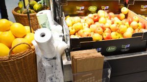 Påsar av alla de slag. Bild av en låda äpplen i en matbutik. Bredvid finns rullar med plastpåsar, biologiskt nedbrytbara påsar samt en låda med bruna papperspåsar.