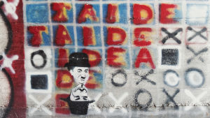 Graffititeos, jossa lukee teksti taide sekä piirrokset Charlie Chaplinin Kulkuri-hahmosta sekä Anonymous-hahmosta Taidekeskus Antareksessa Sippolassa.